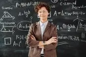 Mathematics teacher standing in front of a blackboard with math formulas written in chalk.